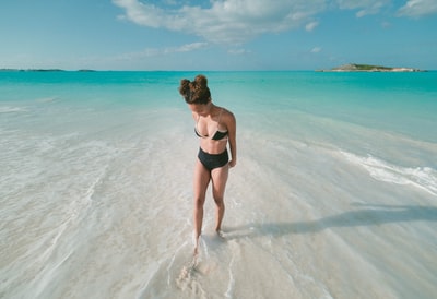 女人穿比基尼泳装,站在沙滩海滨在白天
